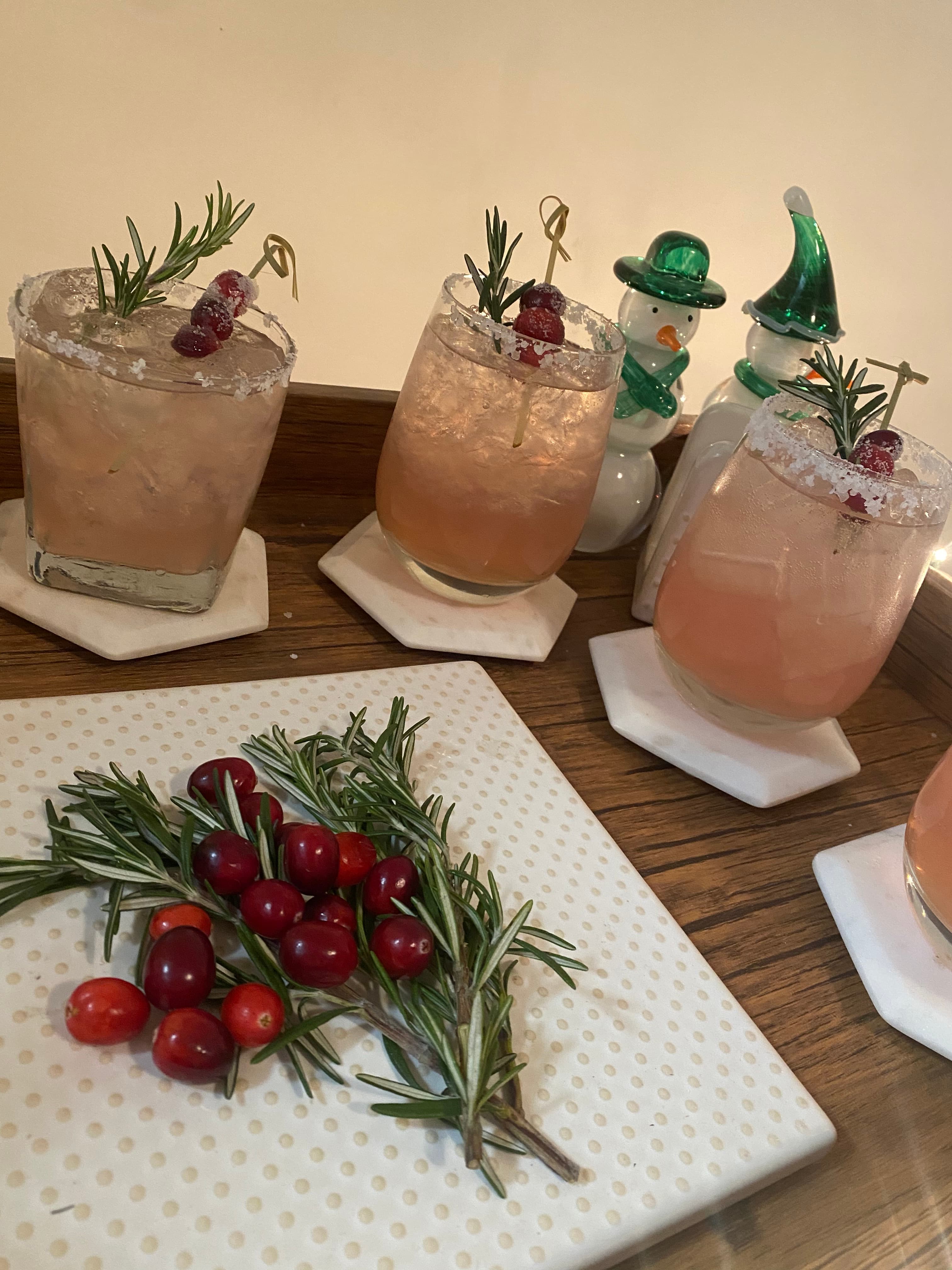 Pink cocktails with rosemary sprigs and cranberries served on coasters.